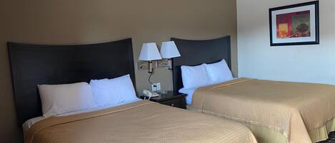 Une chambre d’hôtel avec deux lits, chacun doté d’une tête de lit, d’une table de chevet avec une lampe et d’un tableau encadré au mur.