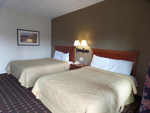 A hotel room with two beds, a nightstand with a lamp, a framed picture on the wall, and a patterned carpet.