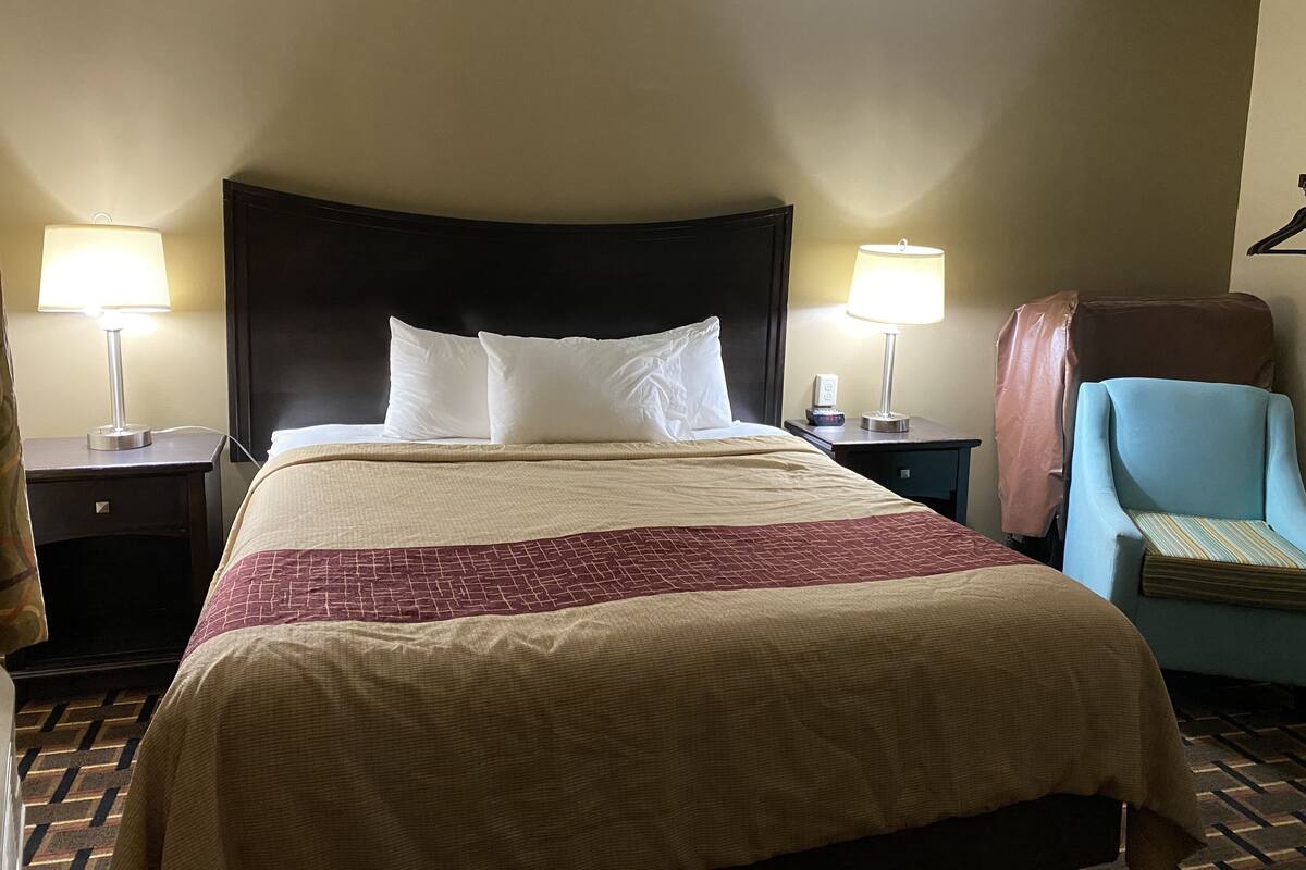 Une chambre d’hôtel avec un grand lit, deux tables de chevet avec des lampes, une chaise et un porte-manteau fixé au mur.