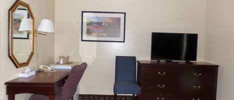 Une chambre d’hôtel comprenant un lit, un bureau avec un téléphone, une chaise, une commode, un téléviseur, un tableau encadré au mur et un sol à motifs.