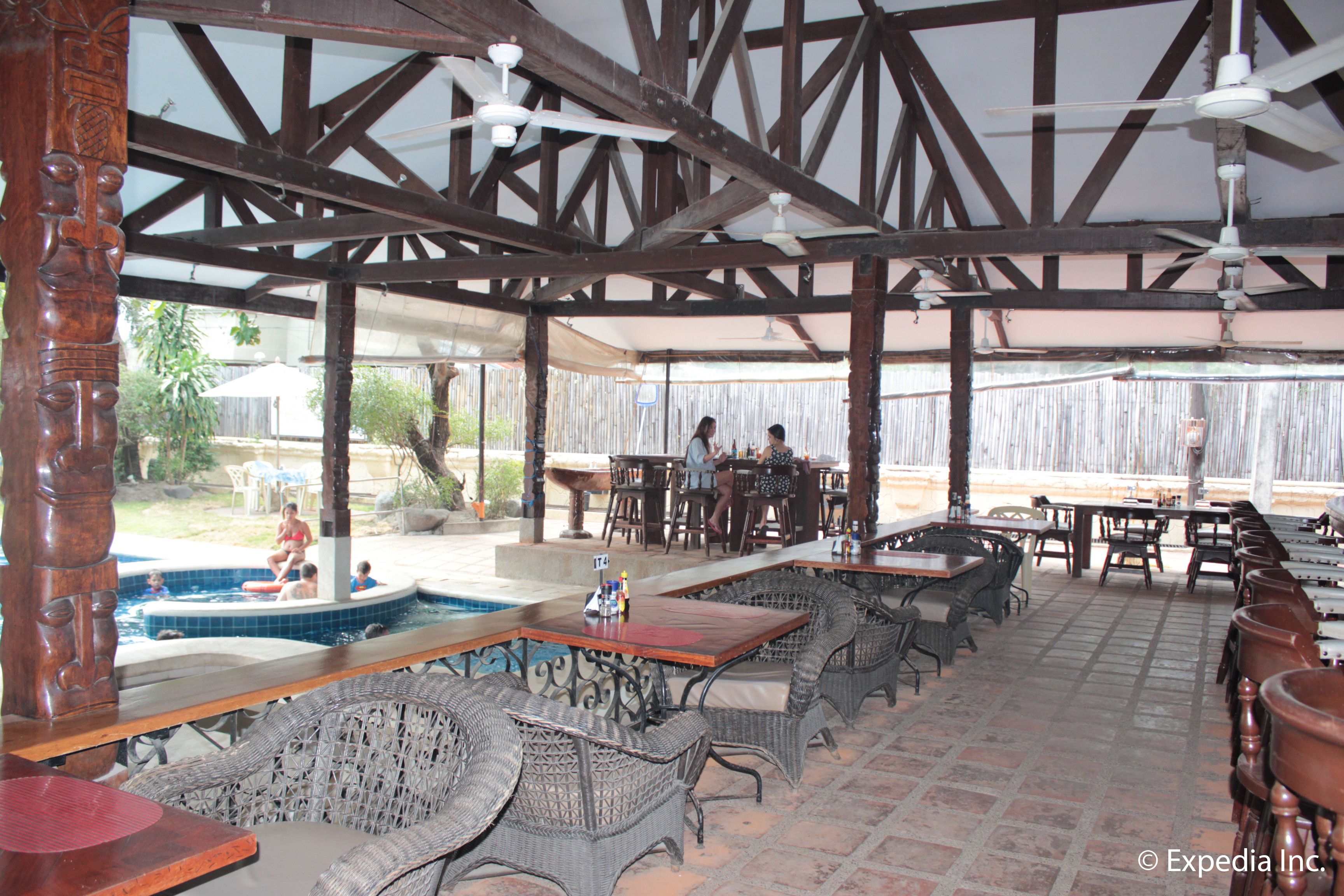 An outdoor restaurant with wicker furniture, a pool, and a covered patio area.