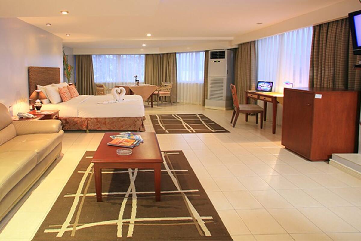A hotel room with a bed, a sofa, a coffee table, a TV, and a desk.
