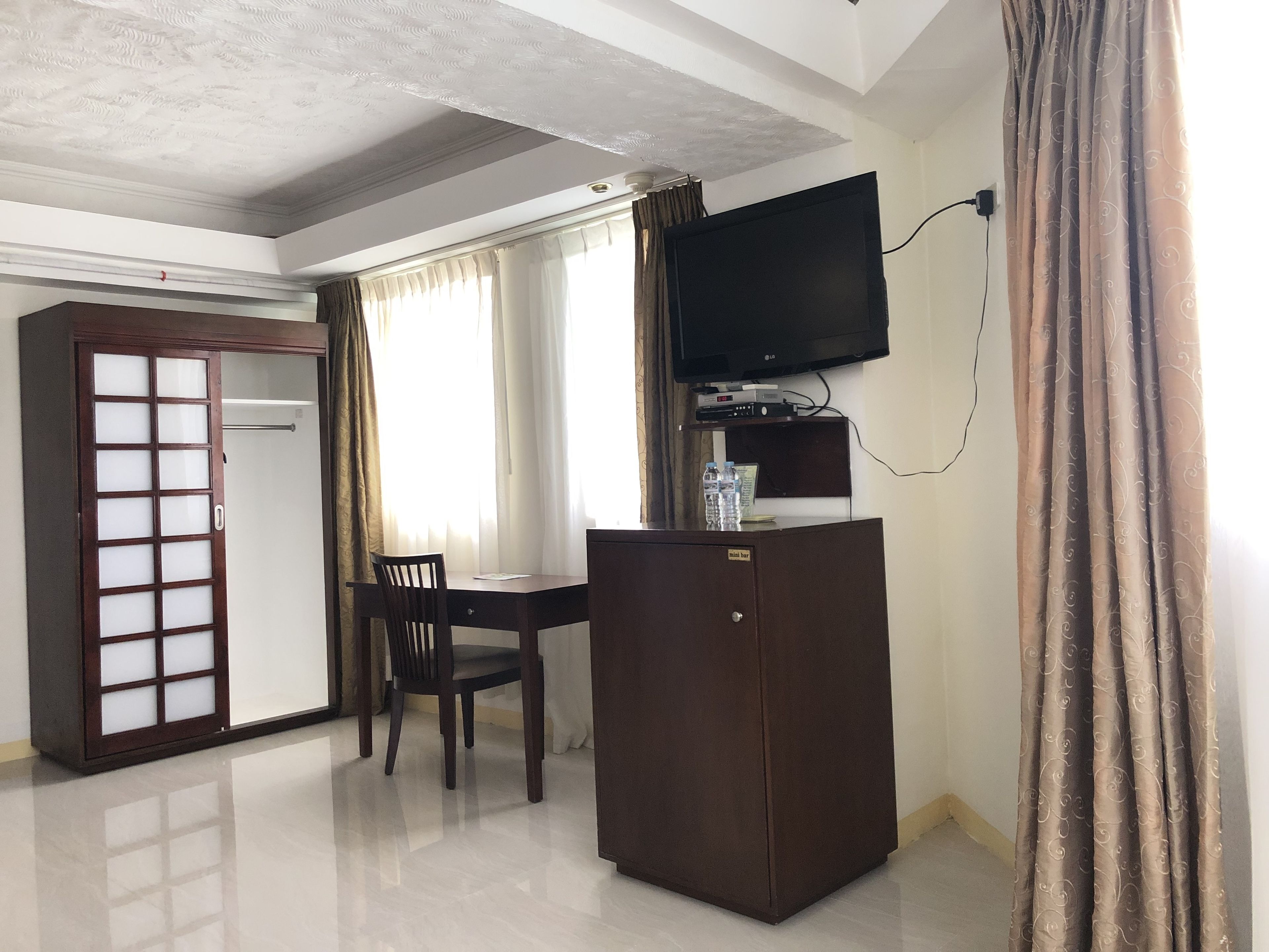 Habitación de hotel con un escritorio de madera, una silla, televisor montado en la pared y un armario.