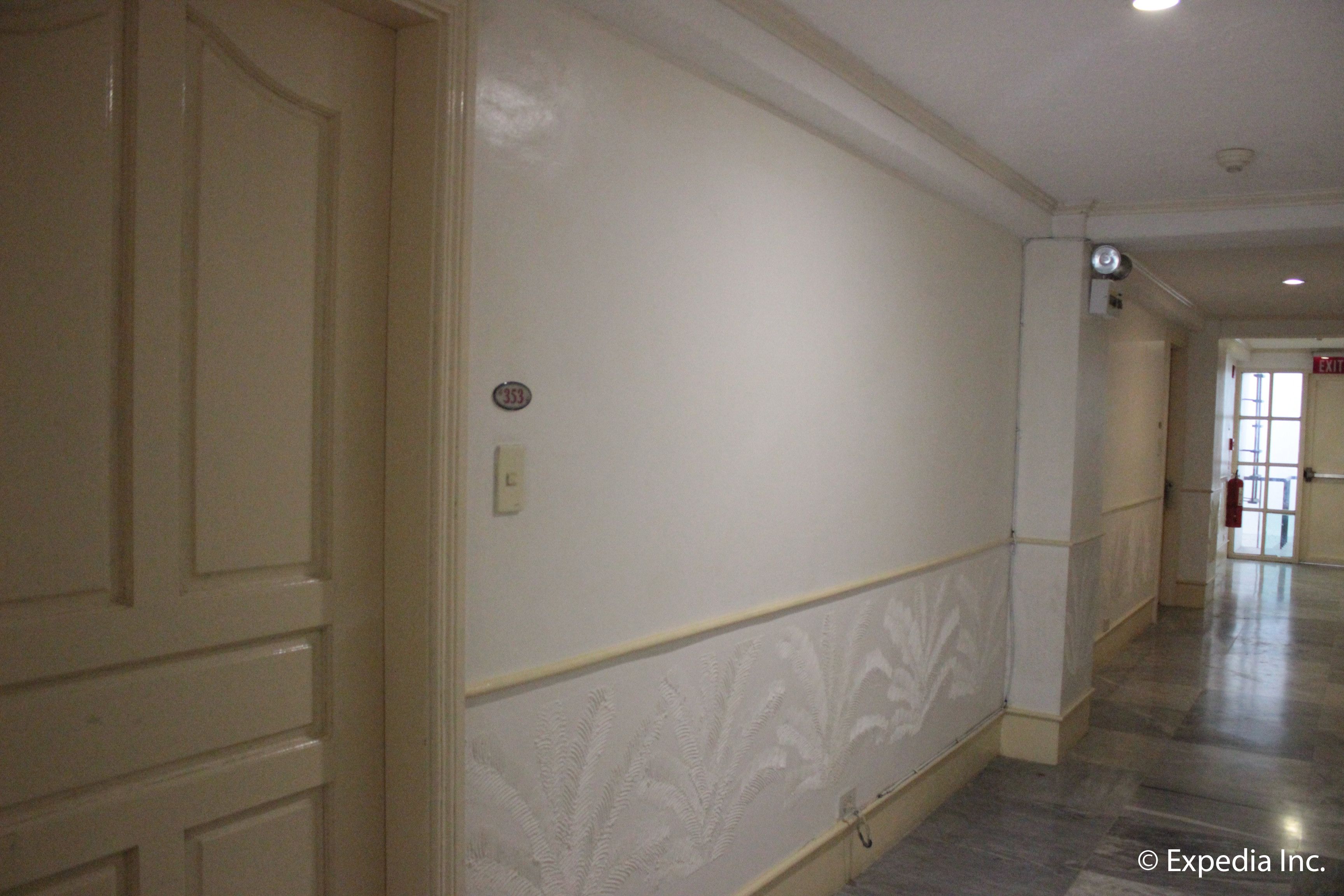 A hallway with a cream-colored door, a wall with a decorative panel, and a tiled floor.