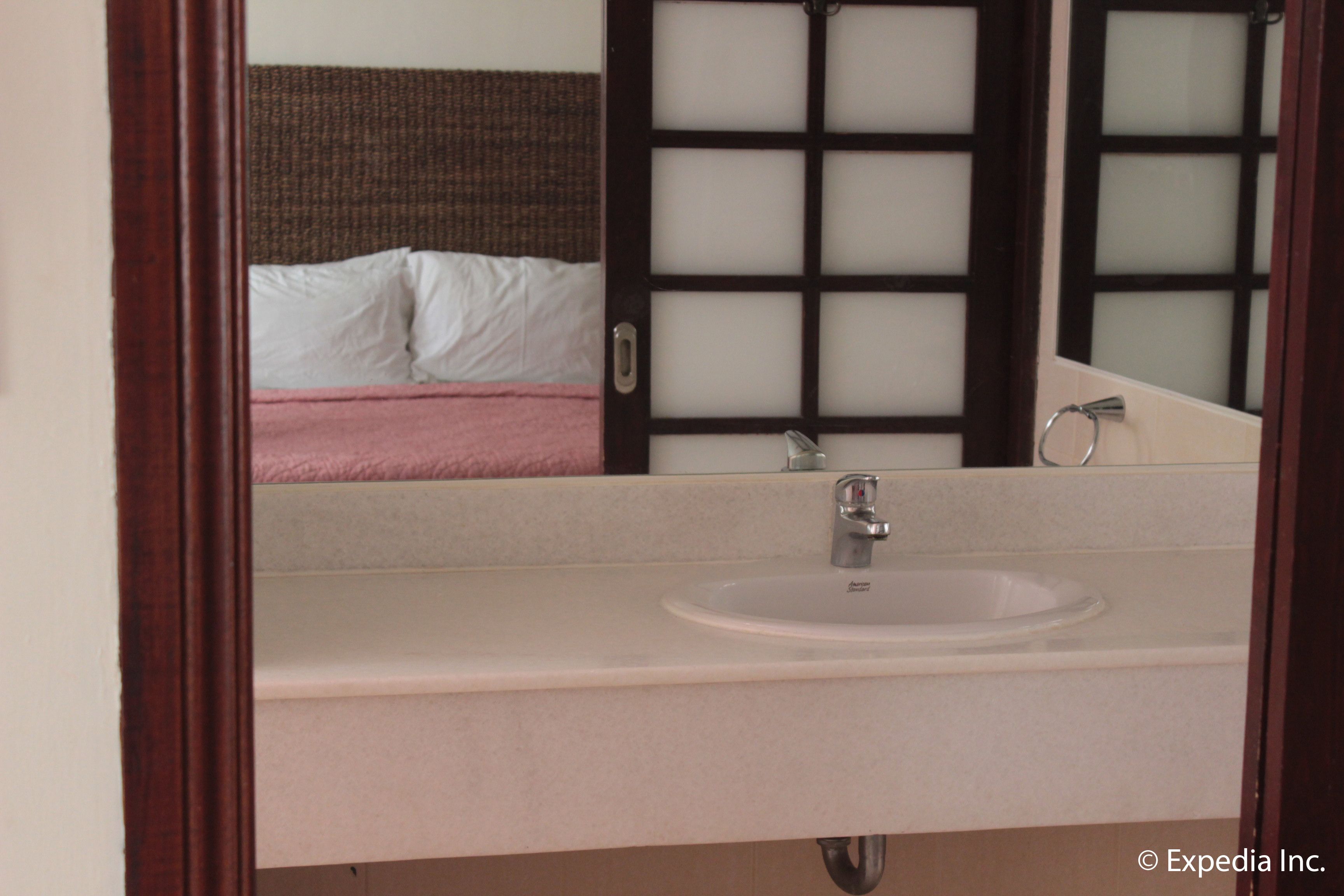 A bathroom with a sink, mirror, and a view of a bed with white and pink bedding.
