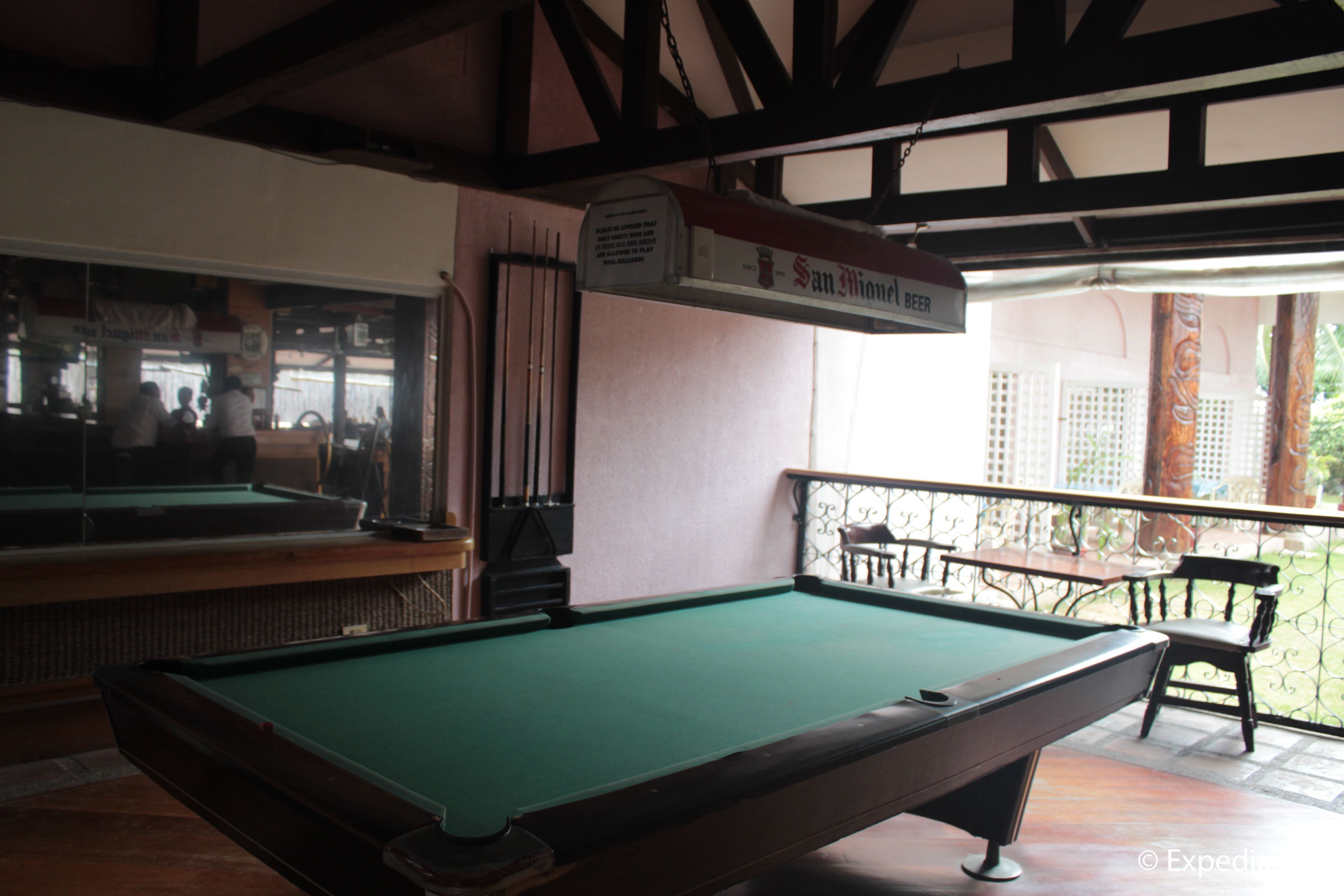 A pool table in a room with a high ceiling and exposed beams. There is a sign above the table that reads "San Miguel Beer."