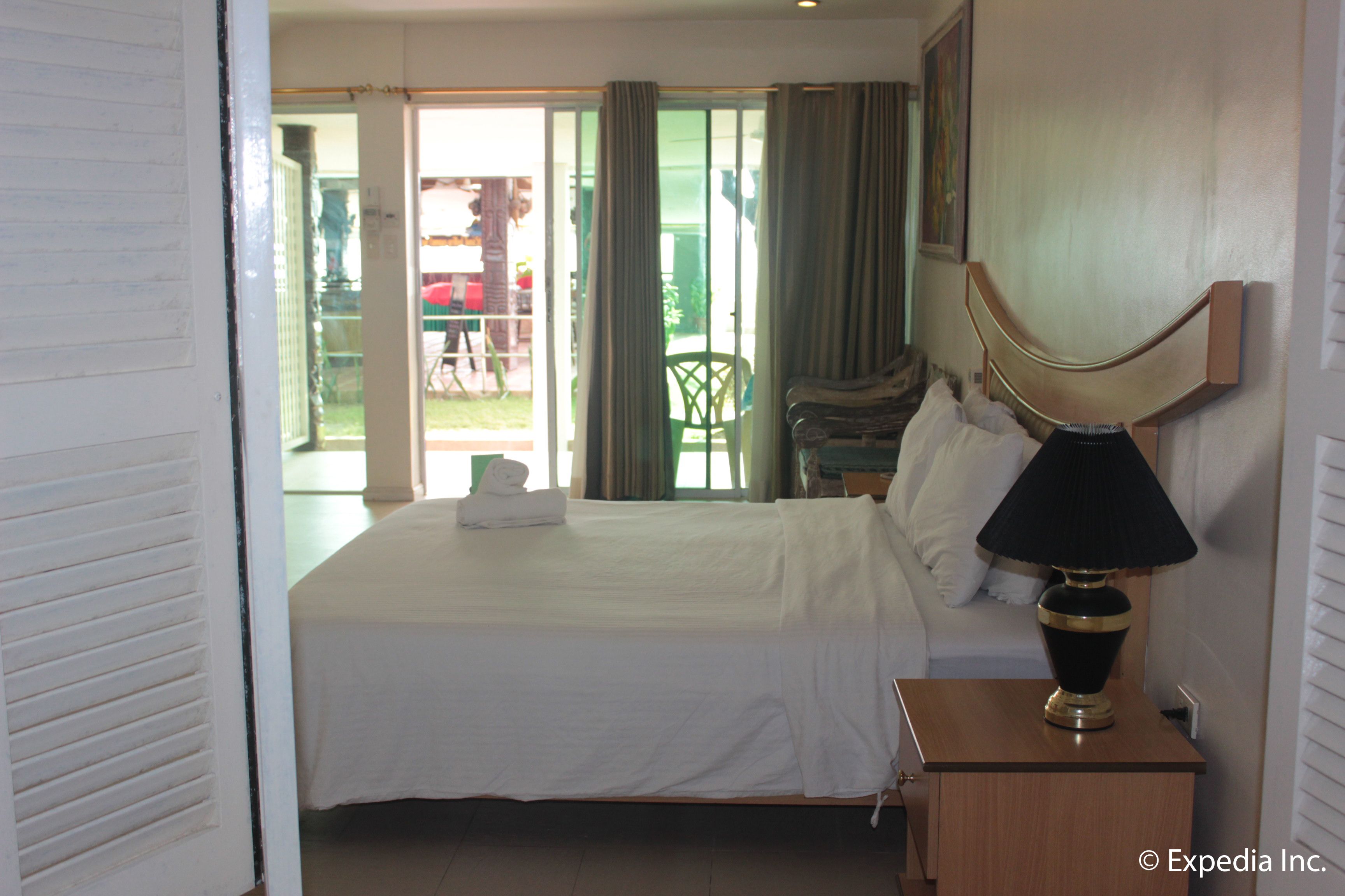 A hotel room with a bed, a nightstand with a lamp, a chair, and a view of the outside.