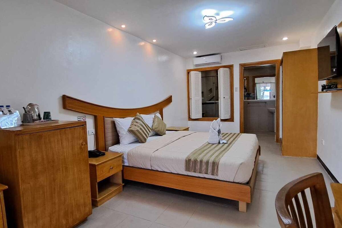 A bedroom with a wooden bed, bedside tables, a wardrobe, a mirror, and a TV mounted on the wall.