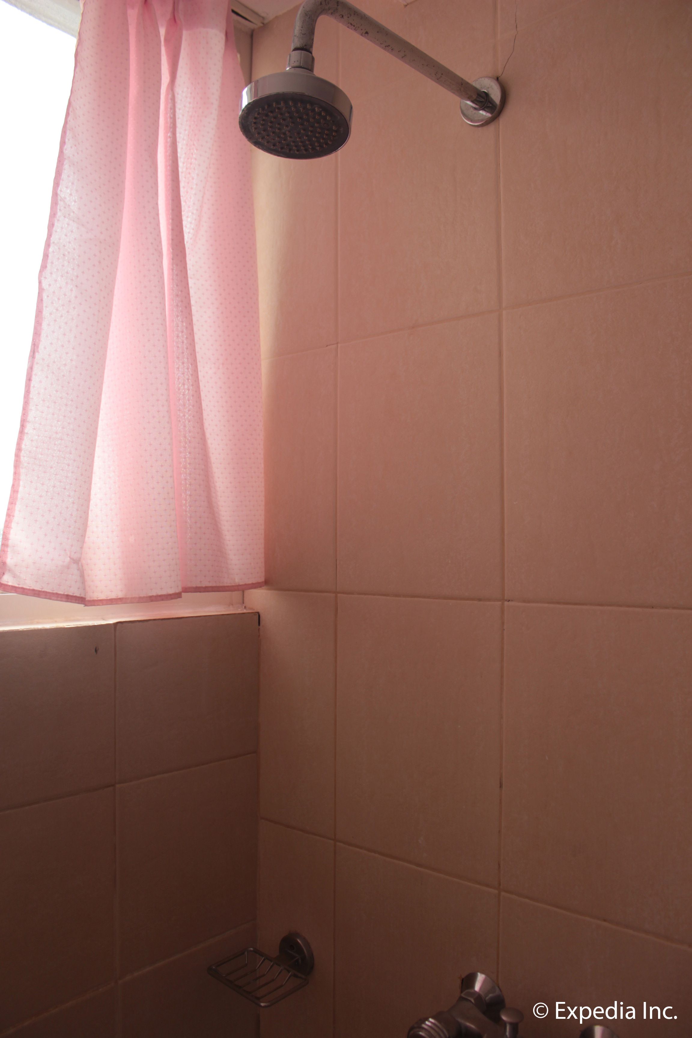 Zona de ducha con azulejos rosas, un cabezal de ducha y una cortina.
