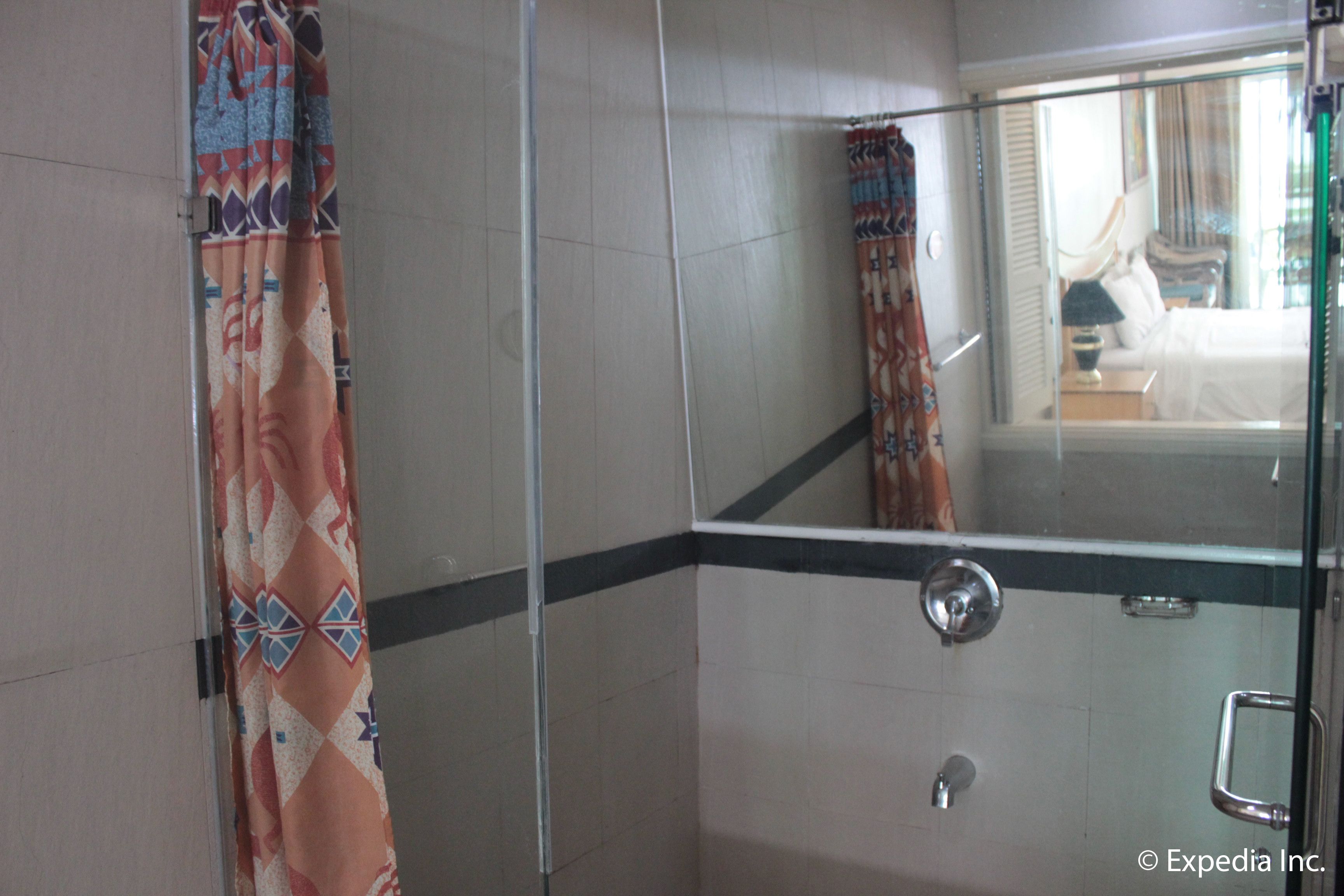 A shower with a glass door, a mirror, and a patterned curtain.