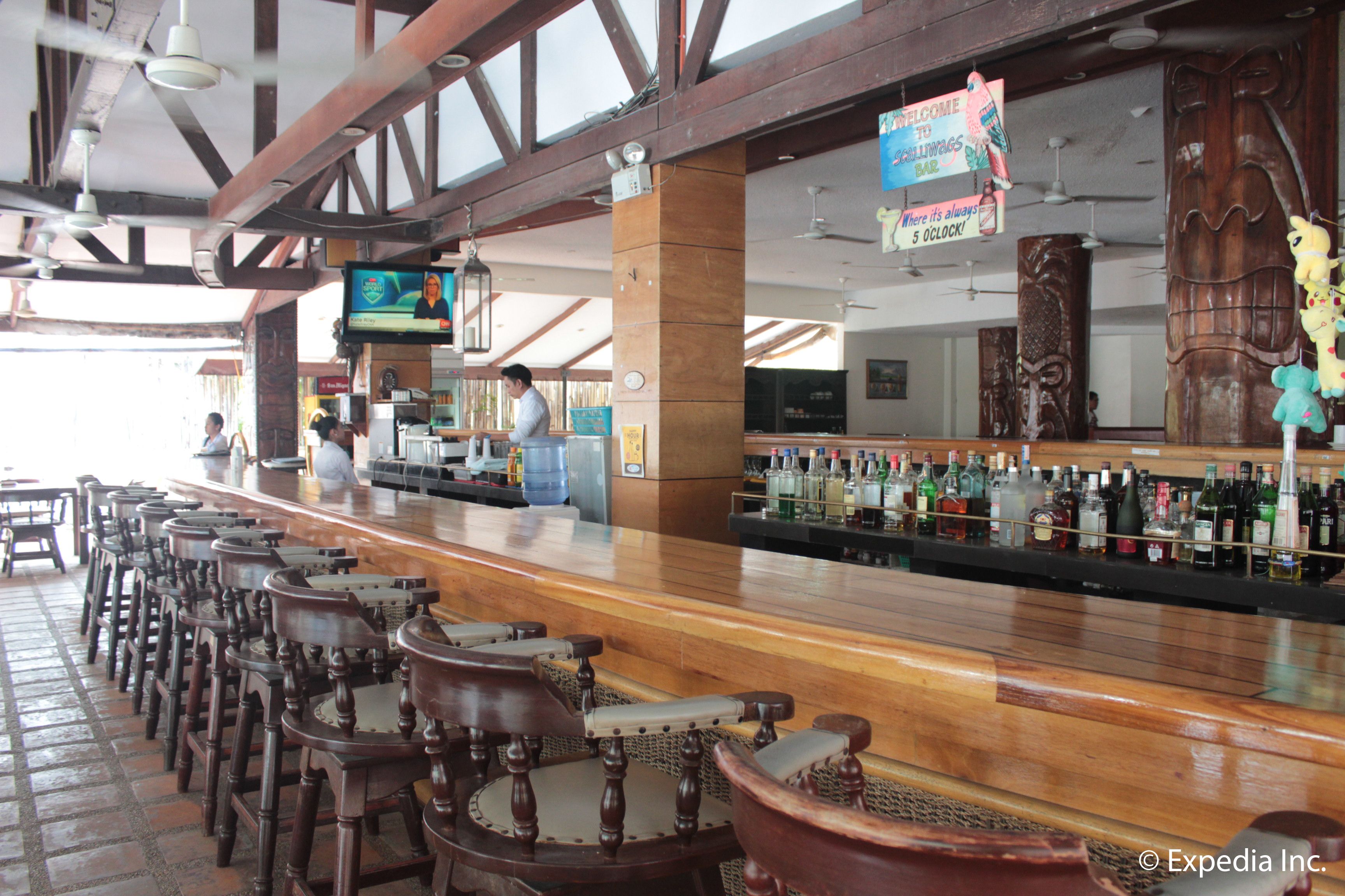 A bar area with wooden chairs, a counter with bottles, and a TV screen.