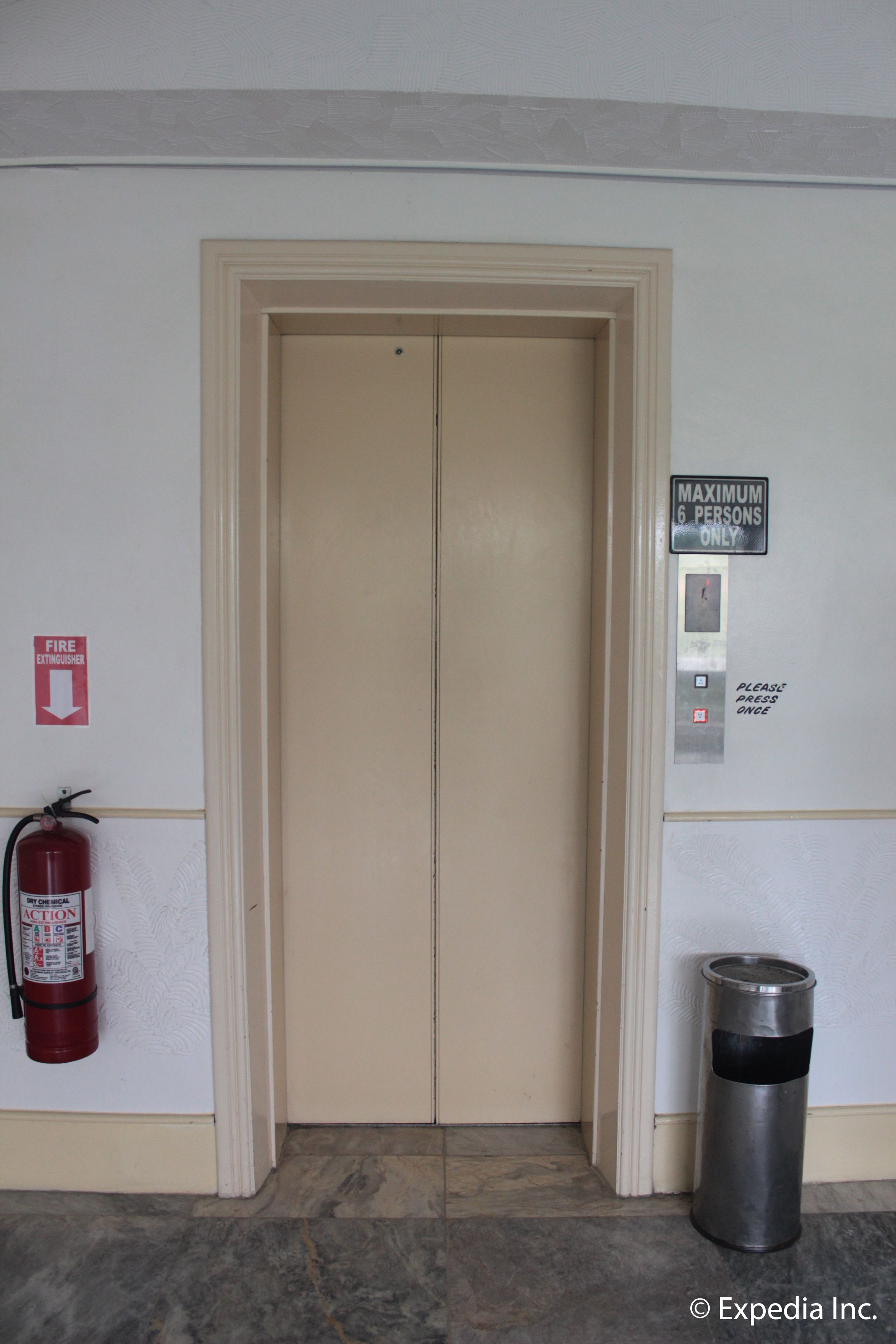 A fire extinguisher, a trash can, and a door with a sign indicating a maximum of 6 persons.