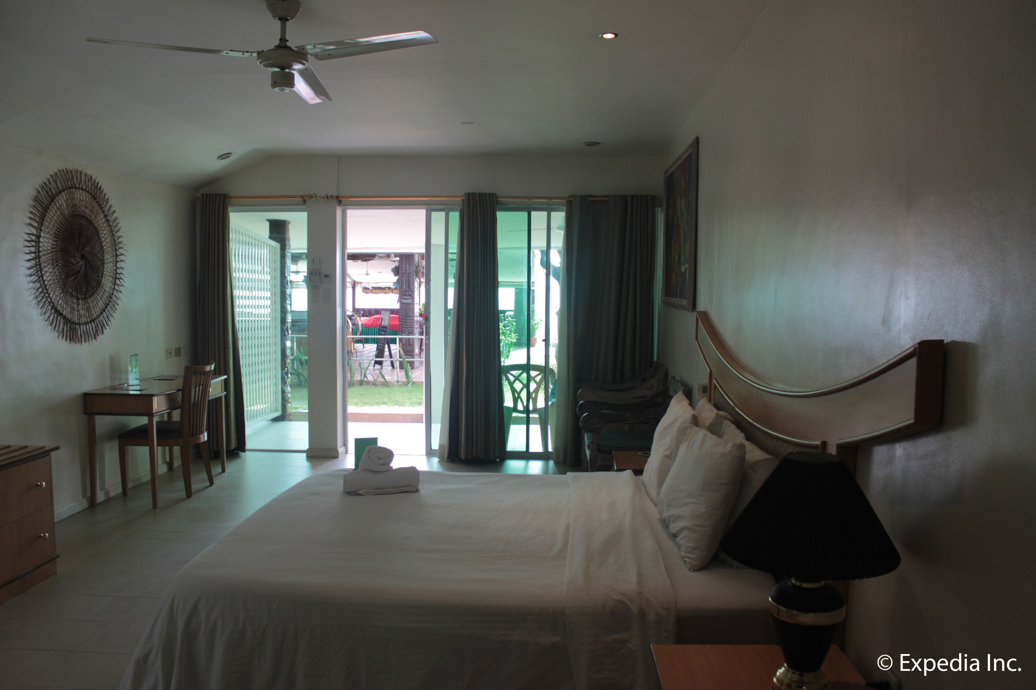 Habitación de hotel con cama, escritorio, silla y ventilador de techo.