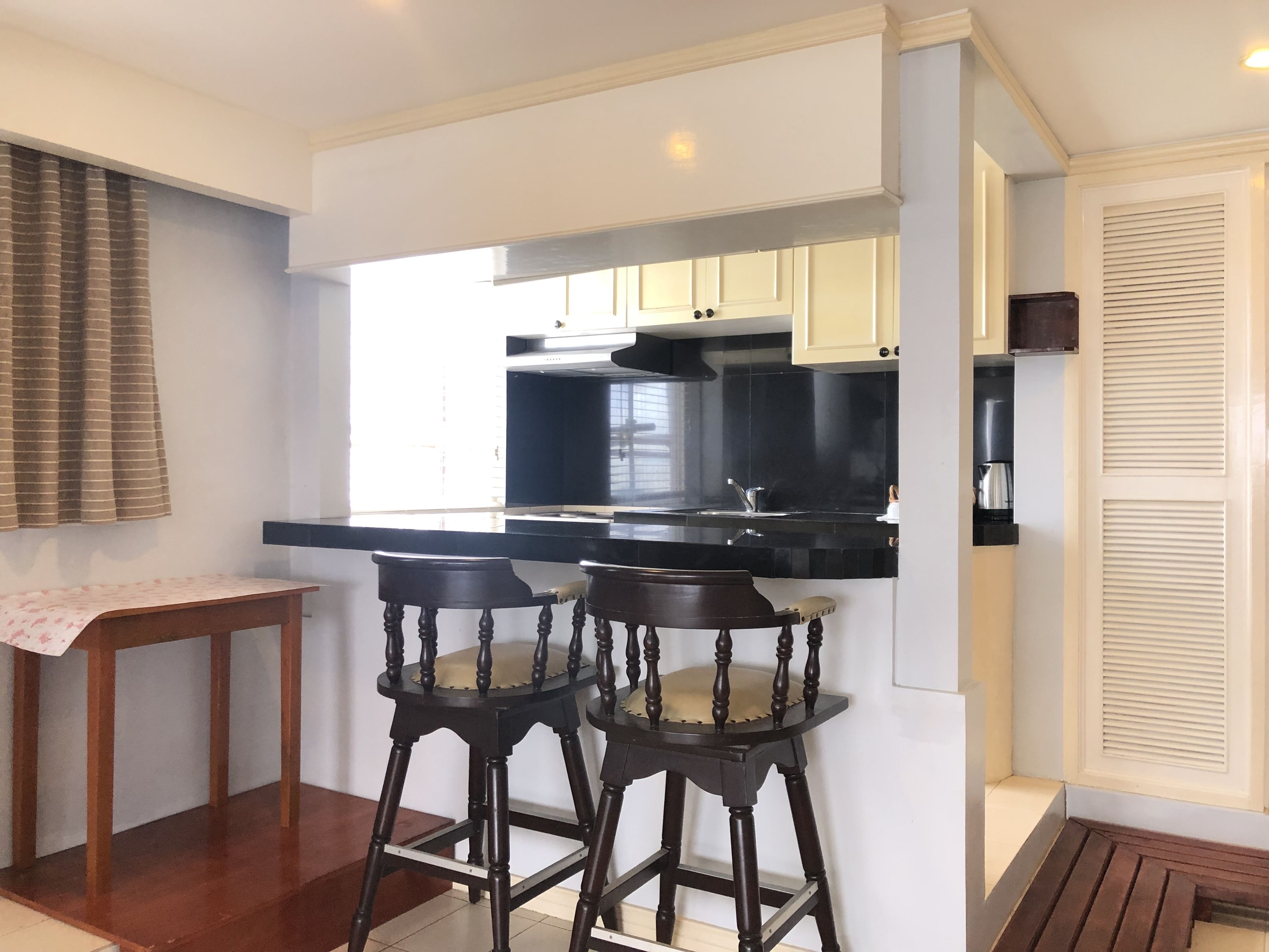 Une cuisine moderne avec des plans de travail noirs, des armoires blanches et une cuisinière encastrée. On y trouve deux tabourets en bois avec des assises rembourrées.