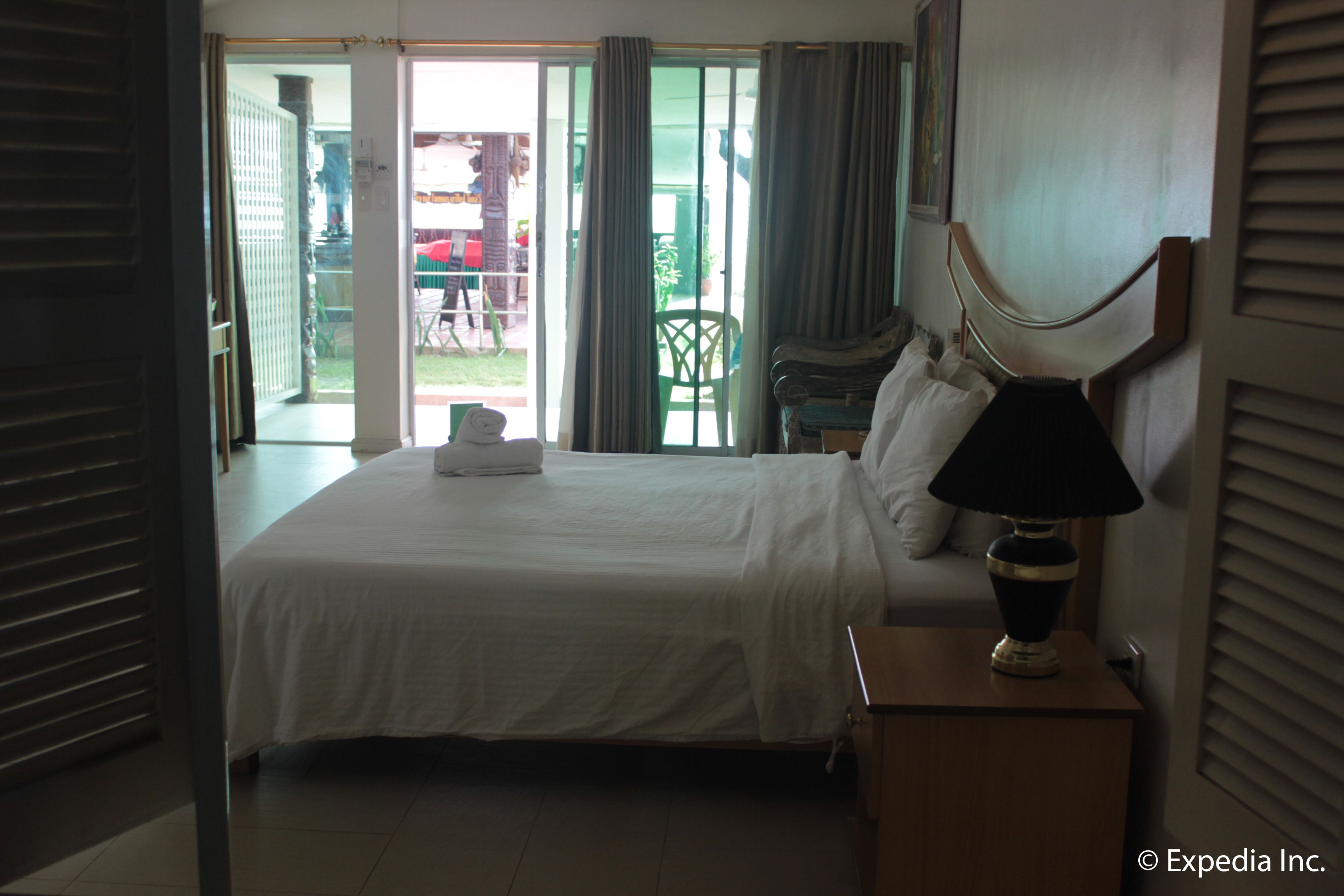 A hotel room with a bed, a nightstand with a lamp, and a view of the outdoor area through a sliding glass door.
