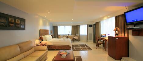 A hotel room with a bed, a sofa, a desk, a television, and a dining area.