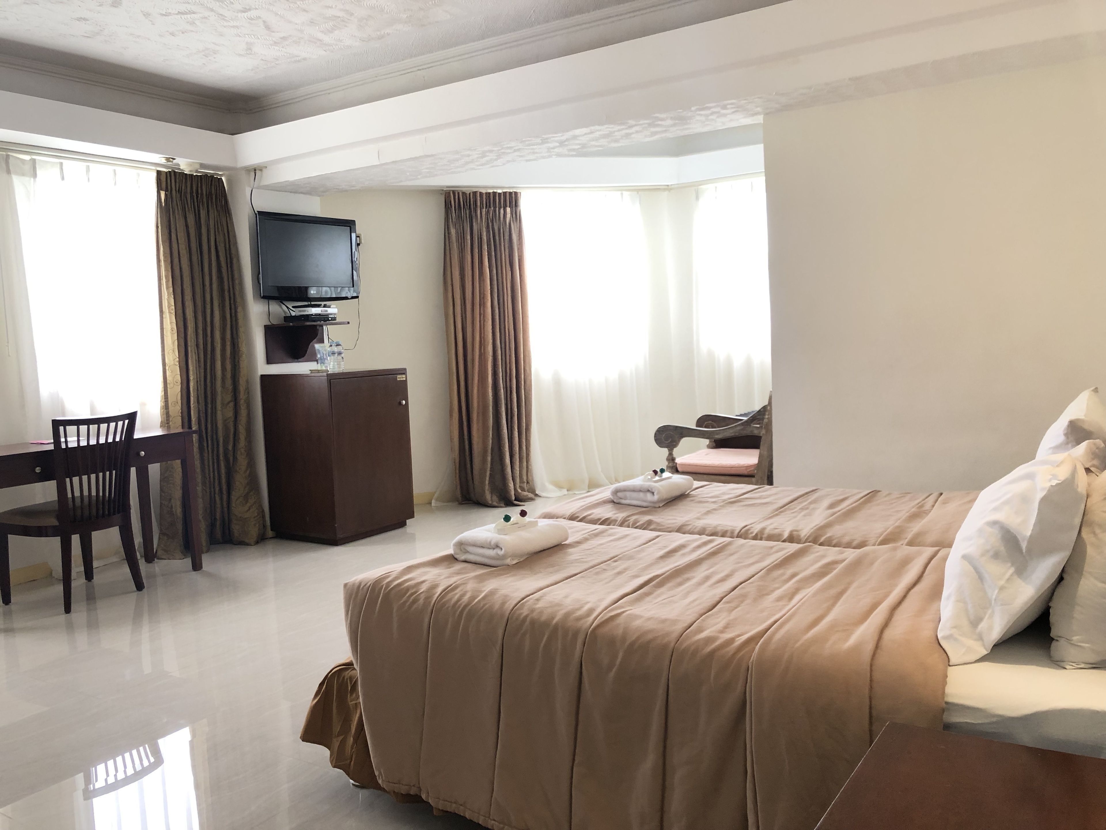 A hotel room with two beds, a desk, a TV, and curtains.
