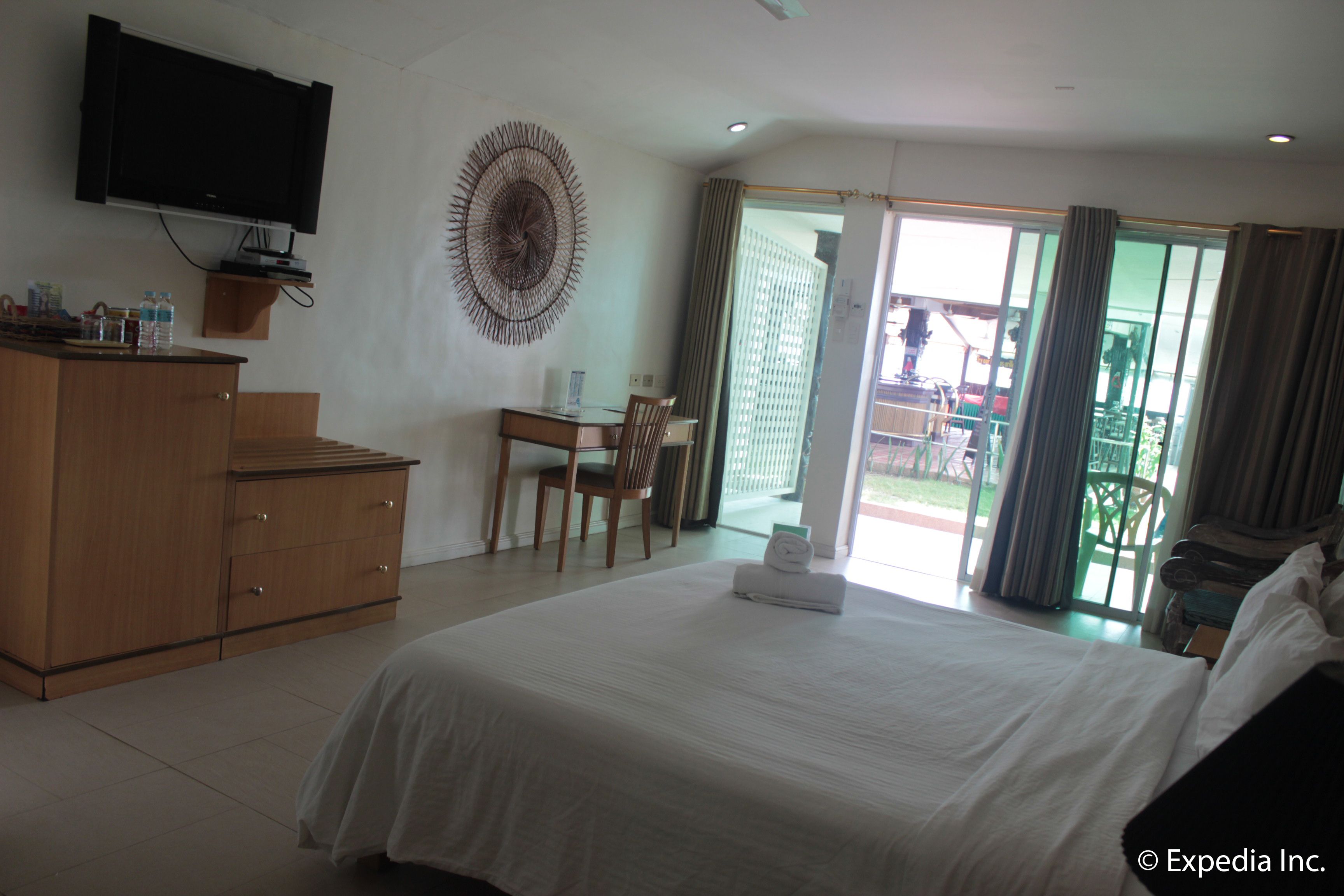 Een hotelkamer met een groot bed, een bureau met stoel, een aan de muur bevestigde televisie en uitzicht door de glazen deur.