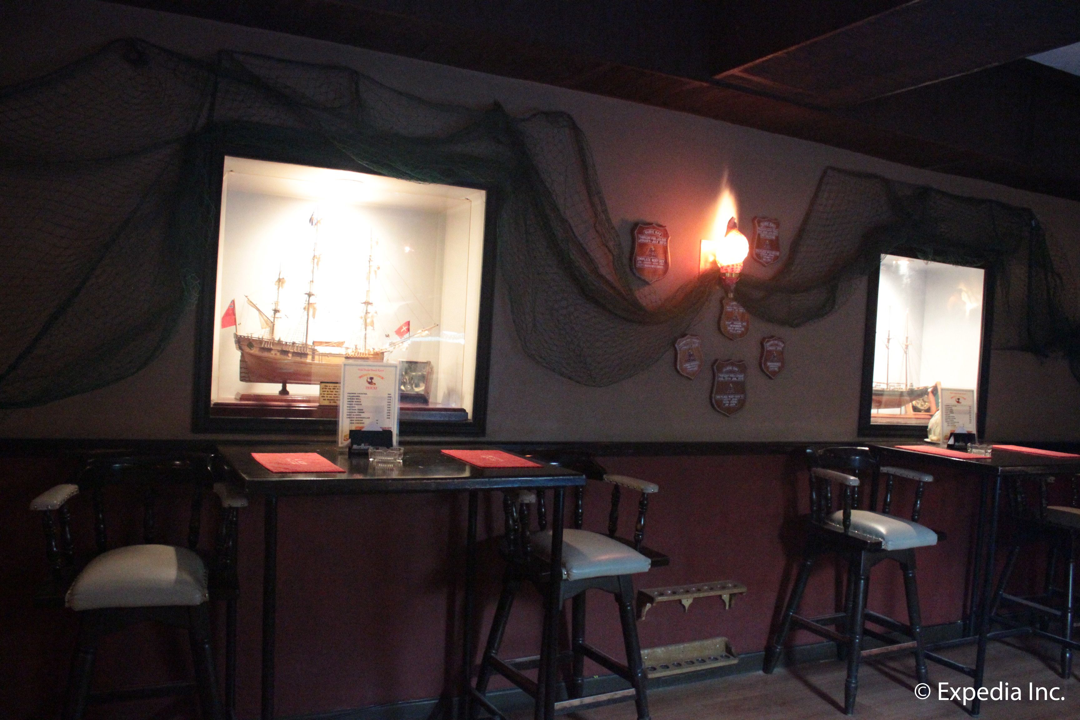 A bar area with a large window displaying a ship, bar stools, and a menu stand.