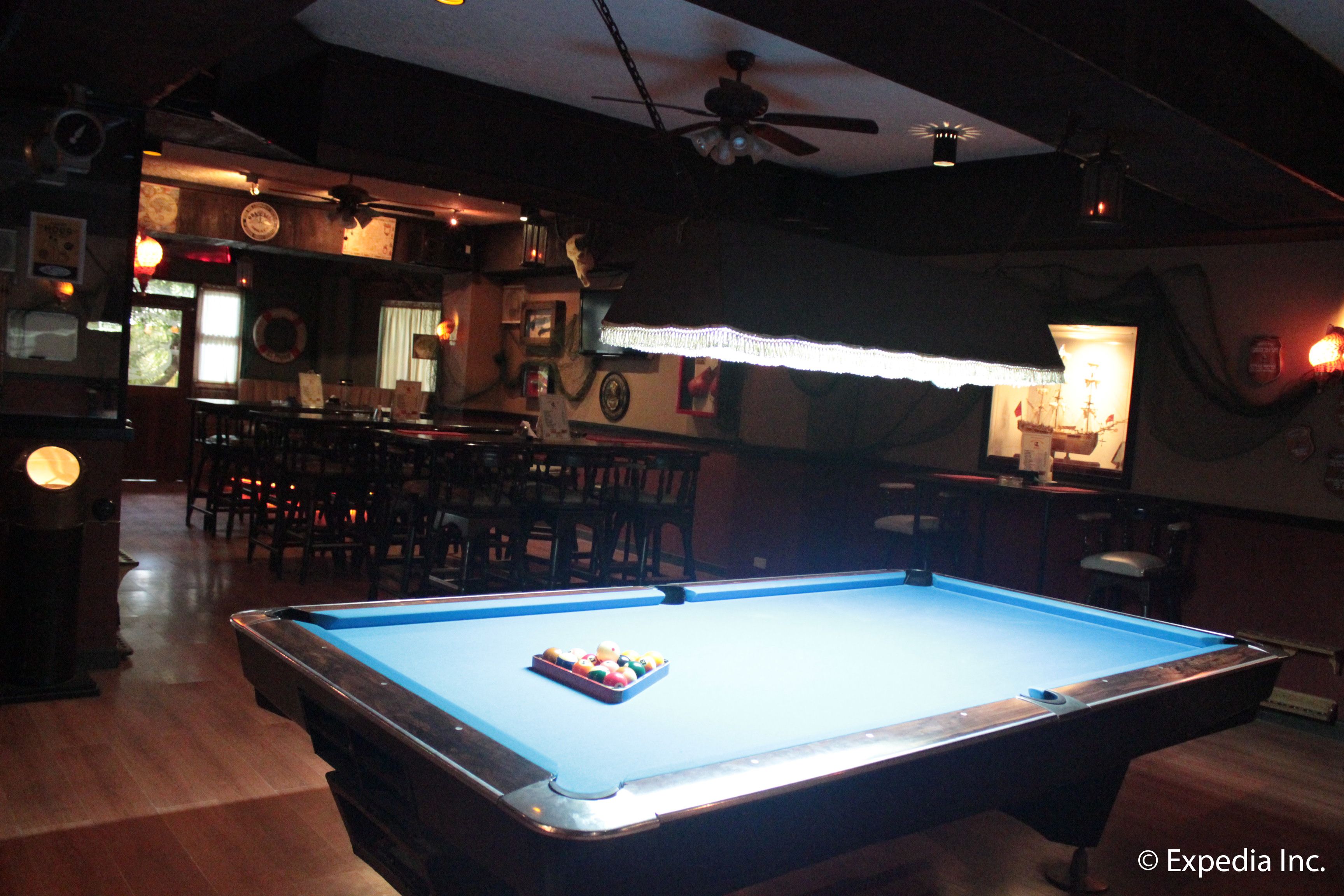 A pool table in a dimly lit room with wooden floors and chairs.
