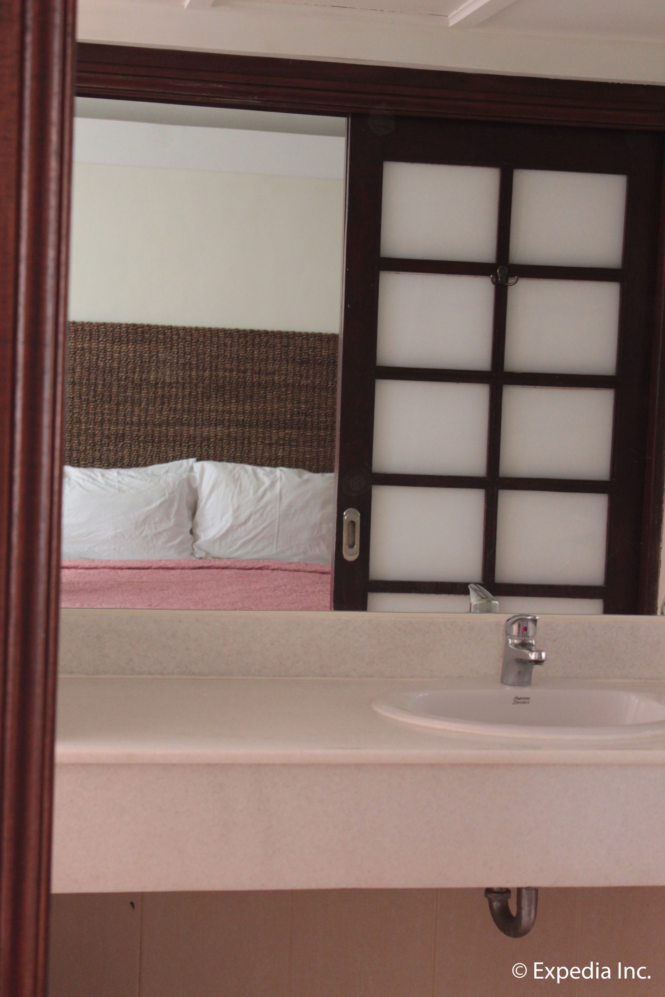 Une chambre d’hôtel dotée d’un grand miroir qui reflète un lit et d’une salle de bain avec un lavabo et une porte en verre dépoli.