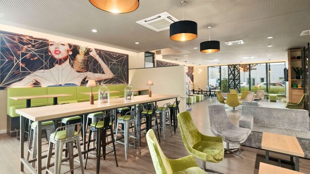 A modern cafe with green and grey seating, a long counter, and pendant lighting. - Super 8 by Wyndham Munich City North (Munich)