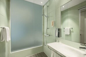 A modern bathroom with a glass shower enclosure, a large mirror, and a white sink.