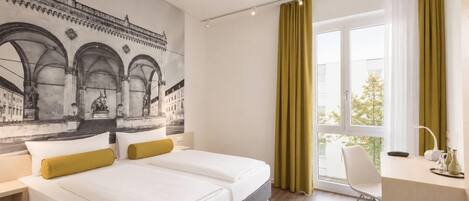 Una habitación de hotel con cama, escritorio y un gran ventanal con cortinas.