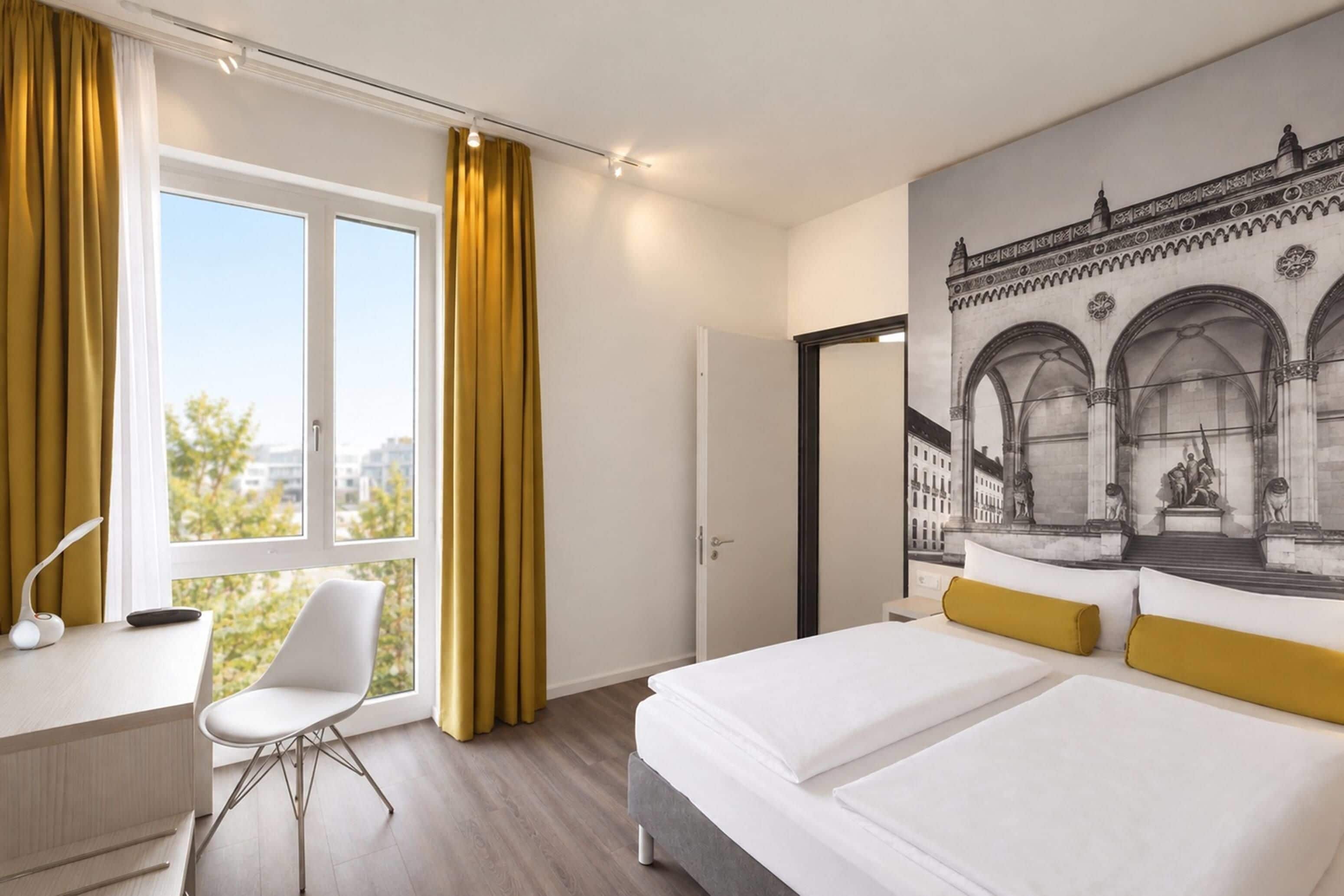 A hotel room with a bed, a desk, a chair, and a large window with curtains.