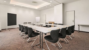 A conference room with a long table, multiple chairs, a whiteboard, and a projector screen. - Super 8 by Wyndham Munich City North (Munich)
