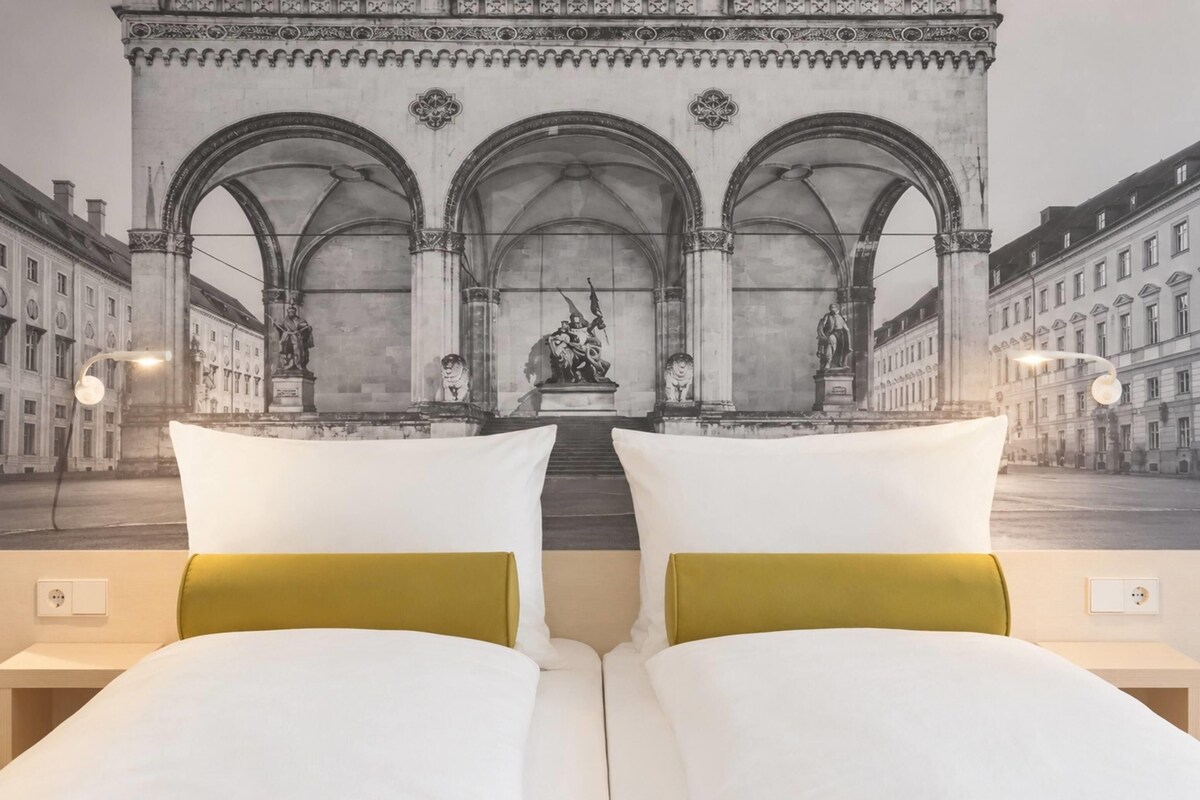 Habitación de hotel con una cama frente a un mural de un arco con estatuas.