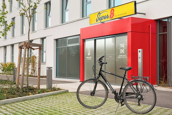 Un bâtiment moderne à la façade rouge, avec un vélo garé devant et une enseigne indiquant un café.
