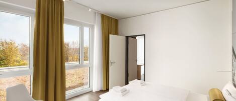 Quarto de hotel moderno com uma cama grande, uma cadeira e vista para o exterior.