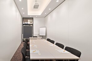 A conference room with a long table, chairs, a whiteboard, and a projector on the ceiling. - Super 8 by Wyndham Munich City North (Munich)