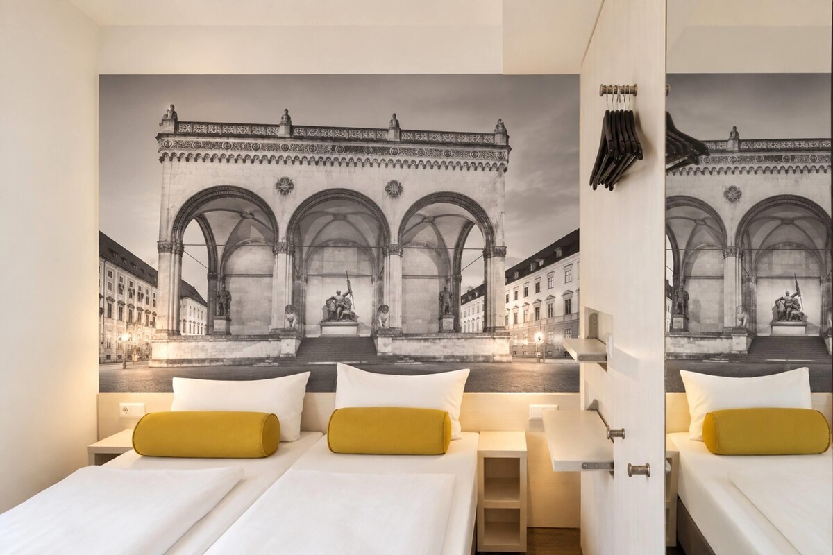A hotel room with two beds, a large mirror, and a mural of a historical building with arches.