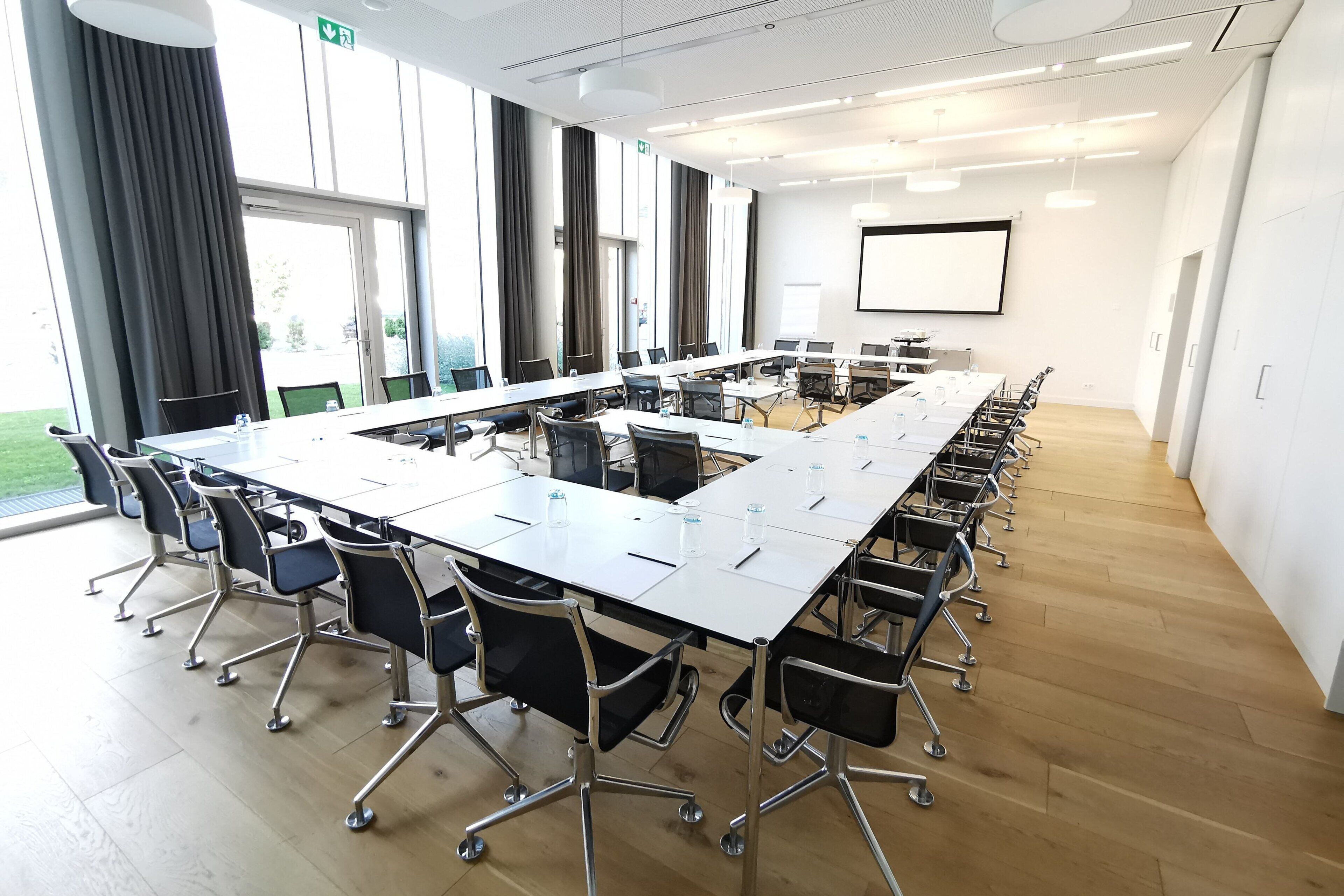 A conference room with a long table, chairs, and a projector screen.