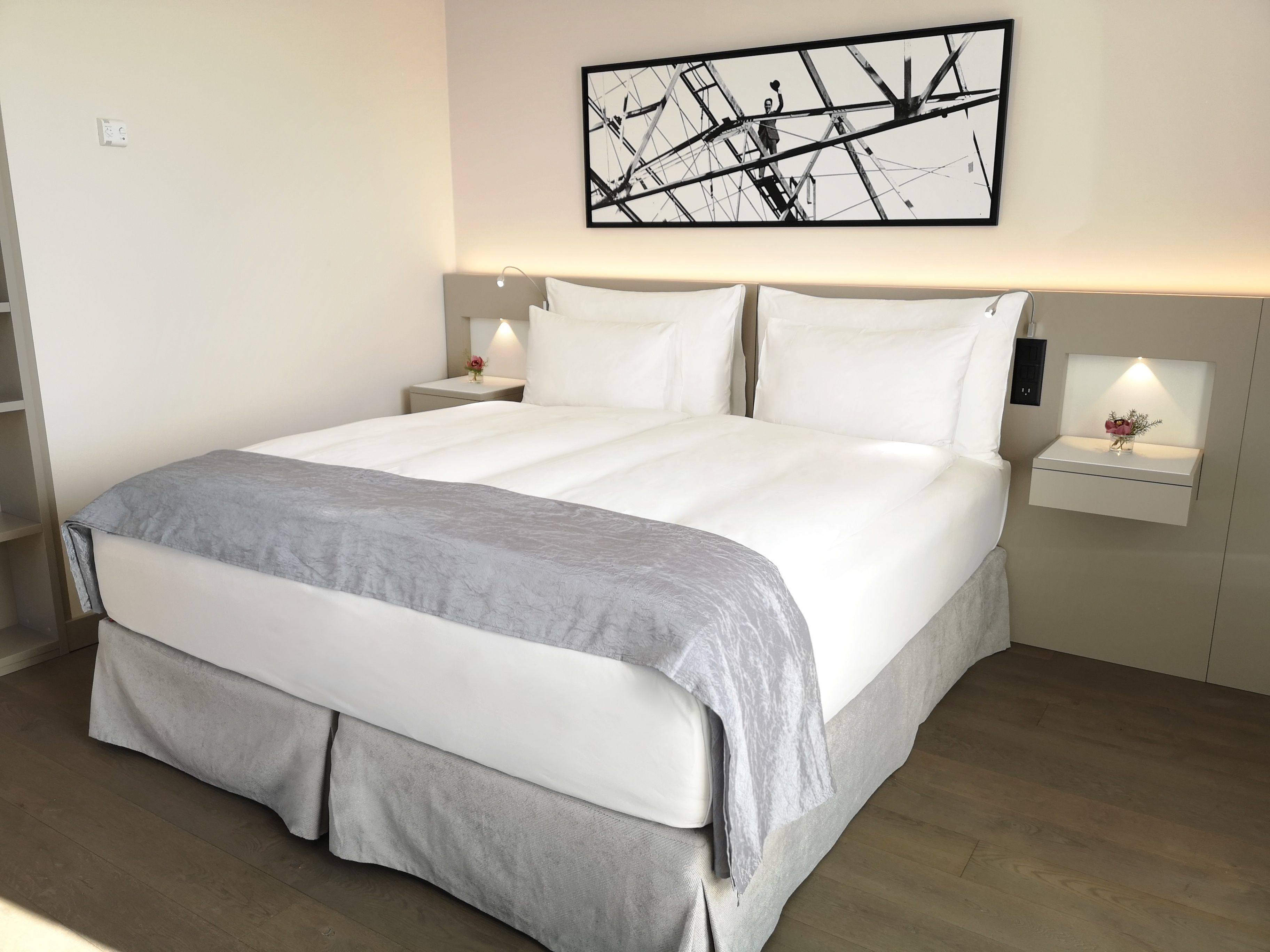 A neatly made bed with a grey throw, a wall-mounted abstract artwork, and bedside lamps.