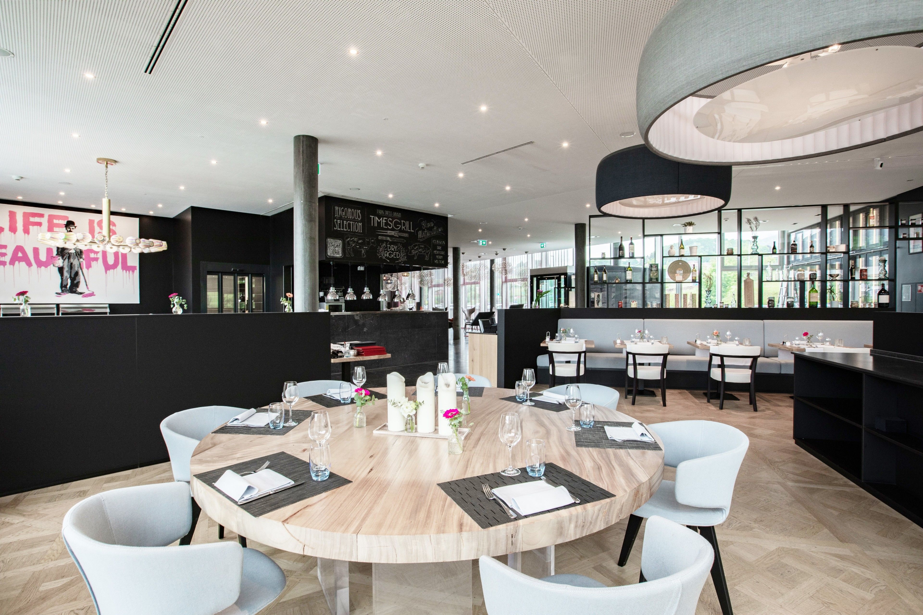 Een modern restaurant met ronde tafels, witte stoelen en een bar met flessen op de planken.