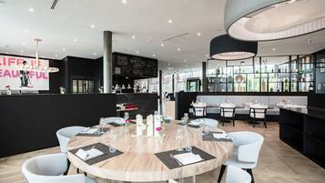 Een modern restaurant met ronde tafels, witte stoelen en een bar met flessen op de planken.