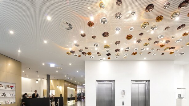 Un vestíbulo moderno con un techo decorado con cristales colgantes, dos ascensores y un mostrador de recepción con una recepcionista.