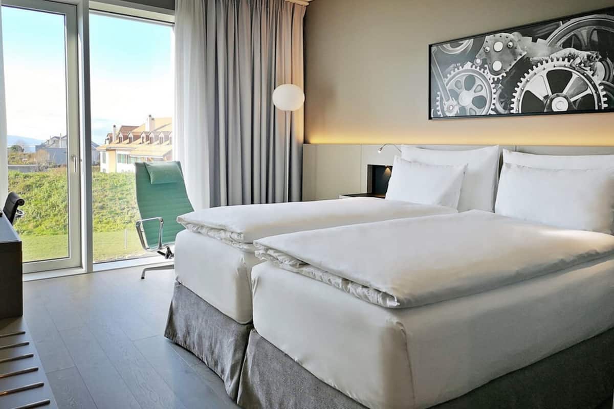 Une chambre d’hôtel avec un grand lit, un bureau, une chaise et une vue sur l’extérieur.