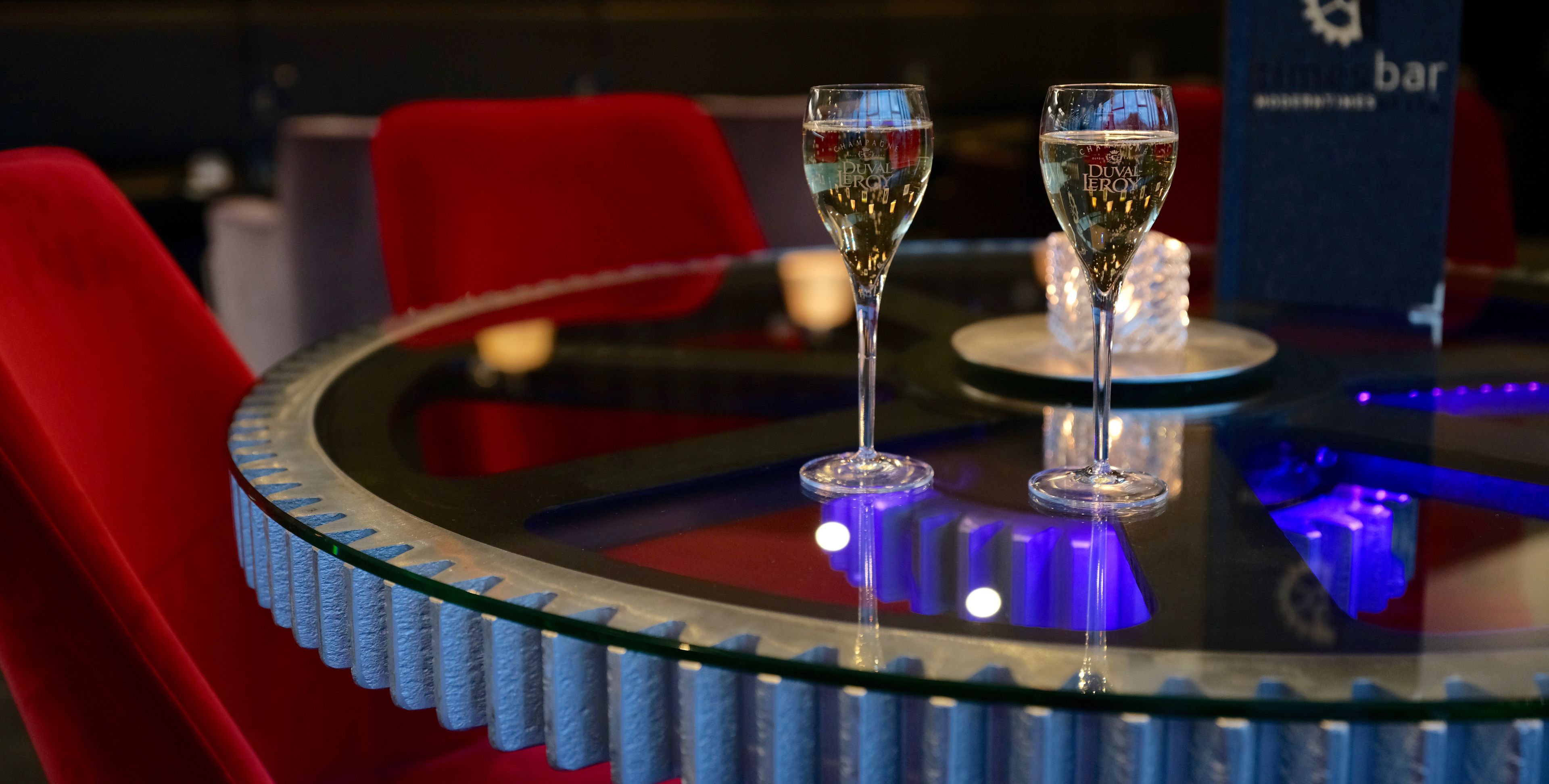 Dos copas de champán sobre una mesa de vidrio iluminada con luz azul.