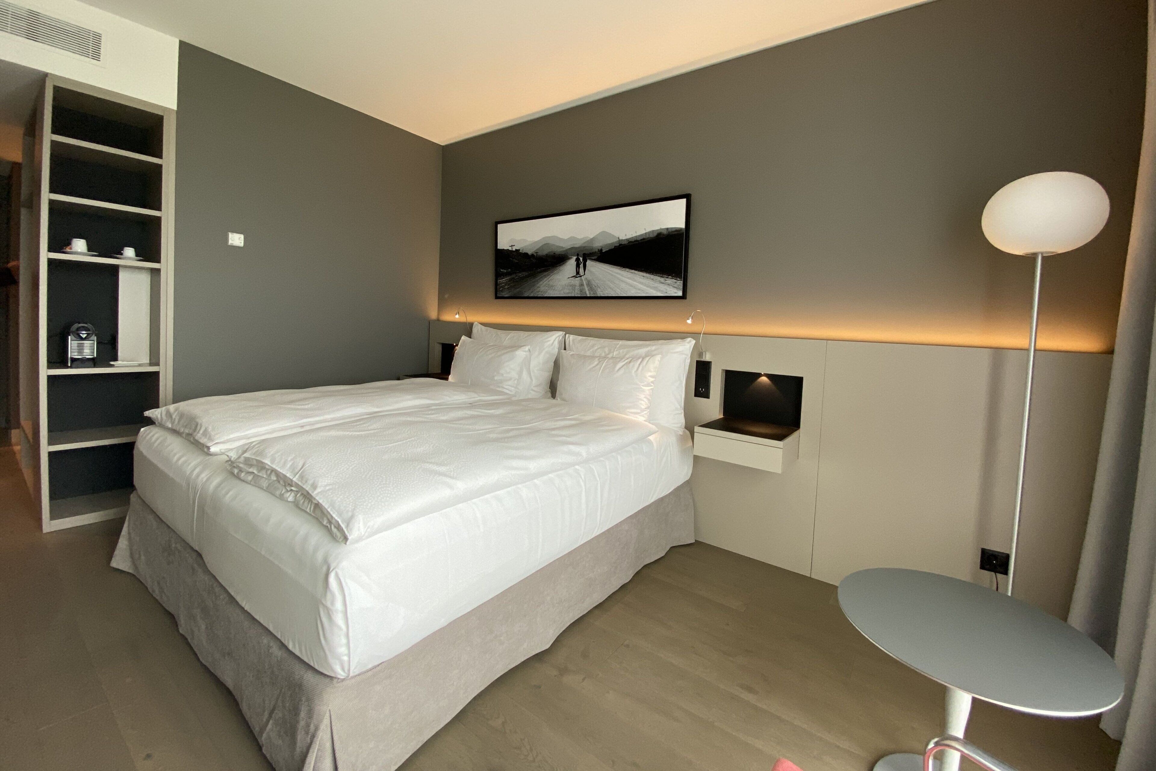 Ein modernes Schlafzimmer mit einem großen Bett, einem Nachttisch, einer Stehlampe und einem Kleiderschrank.