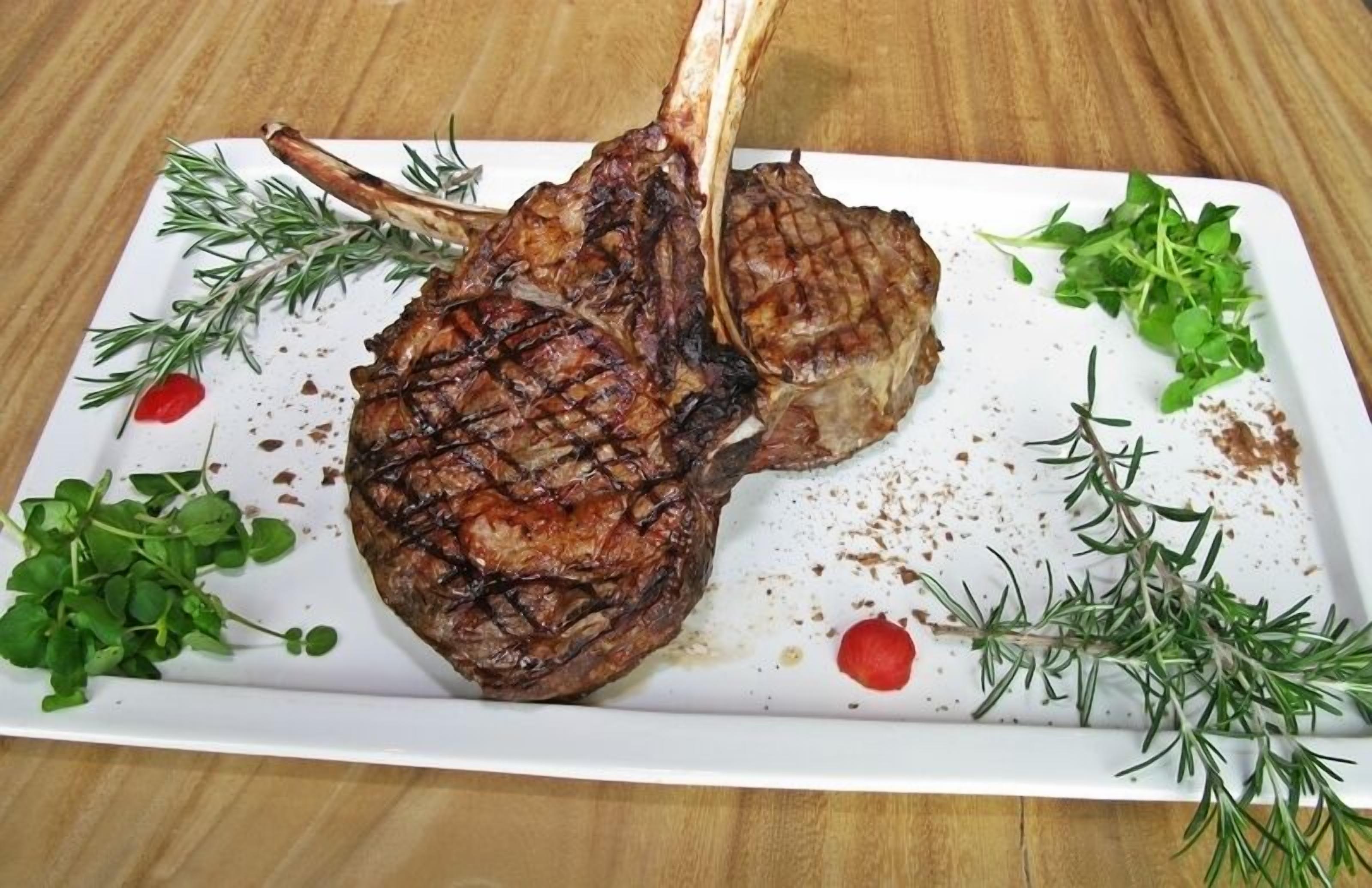 Ein gegrillter Lammkotelett auf einem weißen Teller mit Rosmarin und Mikrogrün.