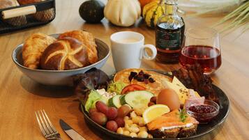 A breakfast setting with croissants, a bowl of salad, a plate with eggs, bacon, and toast, a glass of juice, and a bottle of syrup.