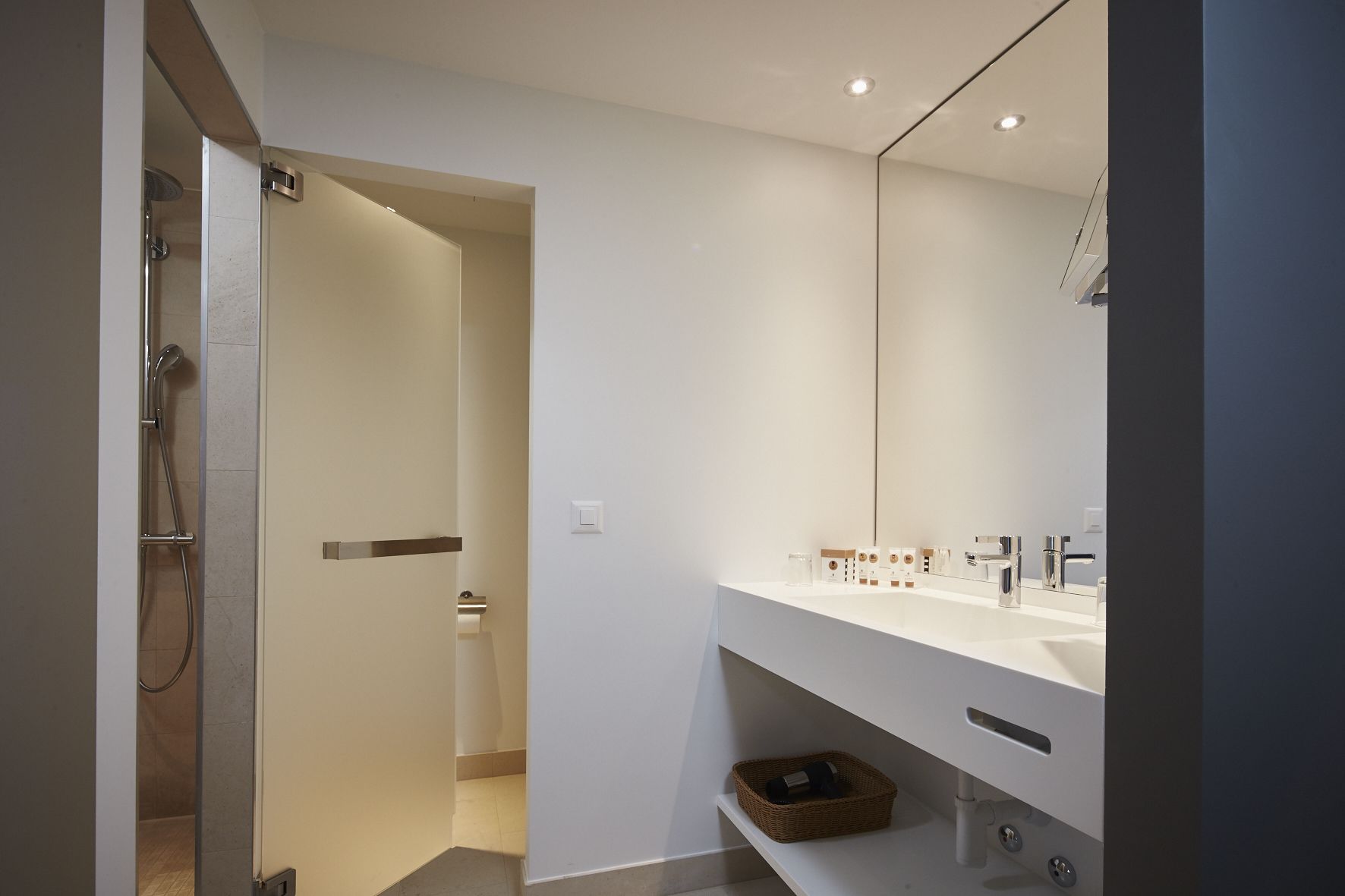 Un baño moderno con tocador blanco, un espejo grande y zona de ducha.