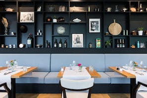 Un restaurant amb interior fosc, taules de fusta i una zona d'asseients amb una banca blaus.