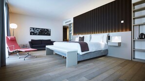 Una habitación de hotel moderna con una cama, una silla roja, un sofá y un estante montado en la pared.