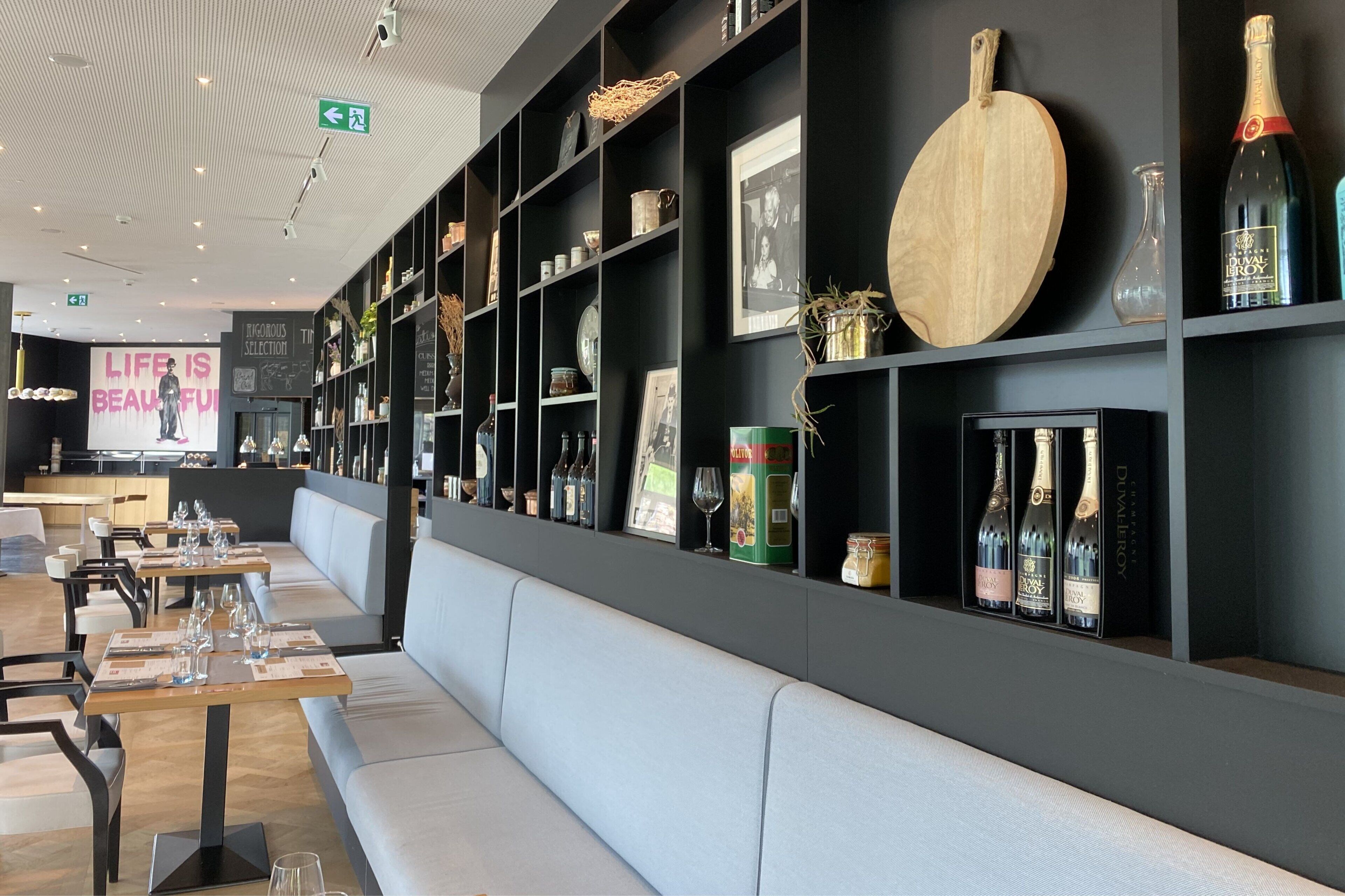 En modern restauranginteriör med högt i tak, svarta hyllor och en lång bänk som används som sittplats.