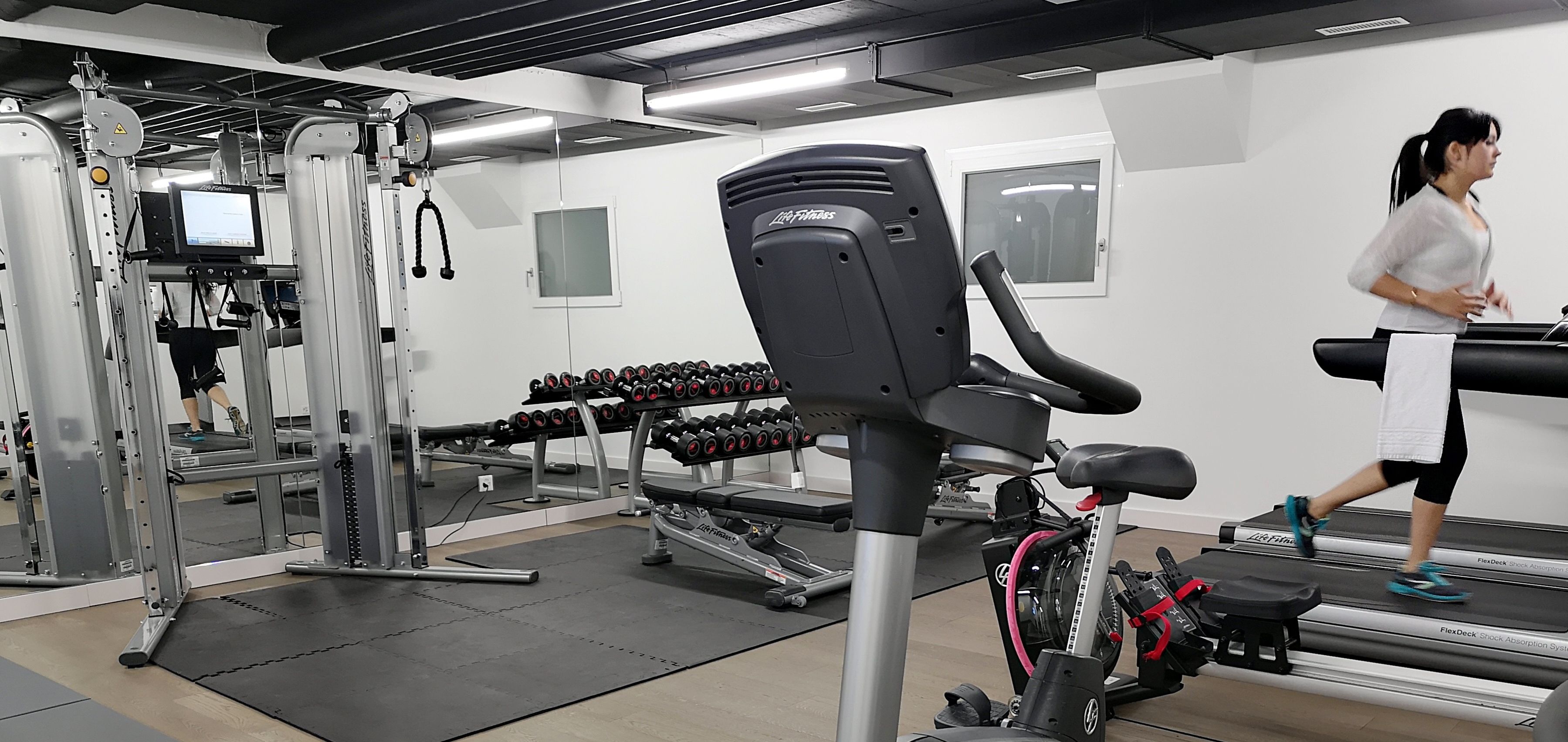 Un gimnasio con equipo de ejercicio, cinta de correr y una persona corriendo.